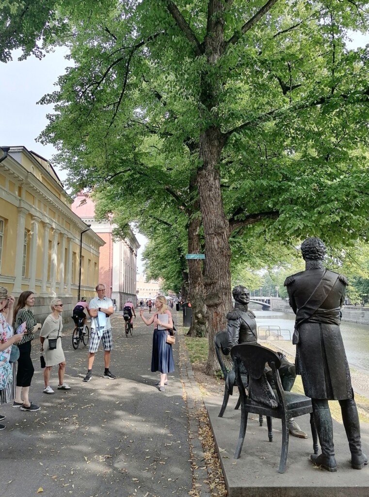 Aurajokirannassa patsaan vieressä opas kertomassa asiakkaille Turun historiasta. Kuva: S.Peltonen